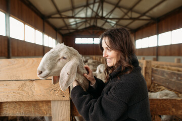 young happy woman on a sheep farm hugging with sheep