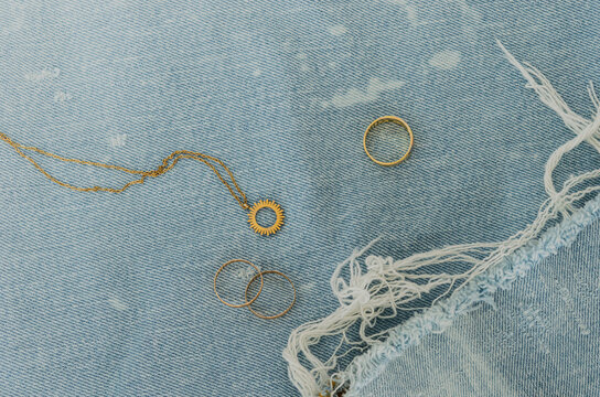 Bodeg&oacute;n con joyas de oro sobre tejido denim azul claro con manchas blancas y flecos deshilachados