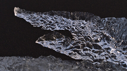 Close-up view of strangely formed iceberg with beautiful clear ice surface shimmering in the evening sun in the black sand of diamond beach in southern Iceland near Jökulsárlón. Focus on center.