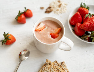 strawberry smoothie with strawberries in a white cup on a white wooden table, decorated with strawberries. Strawberries, cookies near the cocktail mug. Healthy and Vegetarian Breakfast Concept