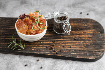 Pieces of dried meat with black pepper and rosemary on a wooden cutting board. Dehydrated product
