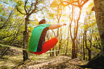Back view A bearded man in age balances while sitting on a taut slackline in the autumn forest....