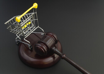 Wooden judge gavel and shopping cart on black table with copy space. Commercial law and consumers rights concept.