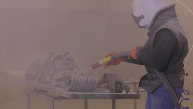 The man is sandblasting the detail. Sandblast metal parts. Sandblasting gun