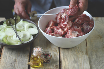 Pieces of raw meat for barbecue and onion rings in a bowl. Hands stir the marinated meat.