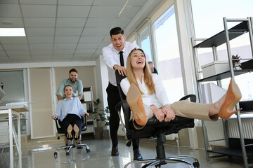 Happy office employees riding chairs at workplace