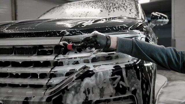 A man in gloves cleans the headlights of the car with a special brush. Car detailing process on a car wash.