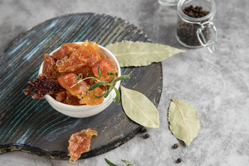 The concept of dehydrated products. On a round wooden chopping board are pieces of dried meat with black pepper rosemary and bay leaf . Copy spase