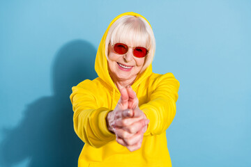 Photo of positive old charming woman hold fingers gun shoot you smile isolated on blue color background