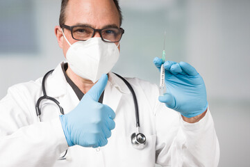 doctor with medical face mask and medical gloves with a pulled up syringe ready for vaccination shows thumbs up