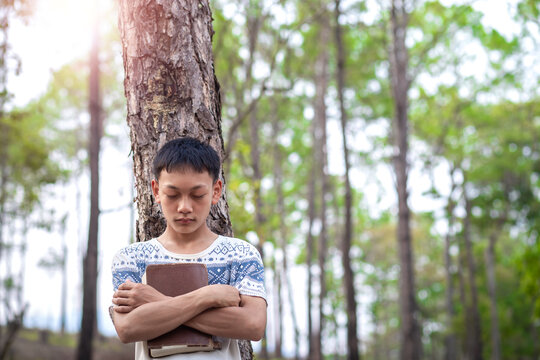Christian boy pray to God with embrace Bible in forest, Focus face.