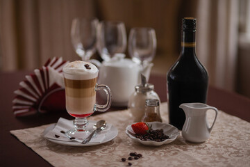 Coffee still life in a pleasant brown and beige color with a coffee drink layers of syrup, cream and coffee, cinnamon, coffee beans, sugar and strawberries