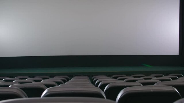 Close up of large blank screen and rows comfortable black seats for visitors in cinema hall. Concept of empty movie theatre.