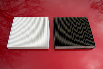 cabin filters on the hood of a red car. the old and new air cleaning filters are located next to...