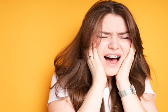 Exhausted Girl With Her Mouth Open Puts Her Hands On Her Cheeks Due To Pain In Her Teeth Due To Braces