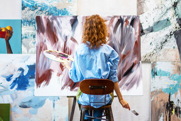 Back view woman artist is drawing abstract picture in workshop studio gallery. Process of creating...
