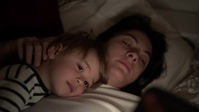 Mother and child lying in bed looking at smartphone at night