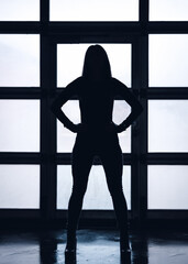 Dark silhouette of a sporty pumped-up girl in full growth against the background of the entrance to the hangar