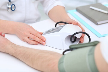 Doctor checking blood pressure of man in clinic, closeup