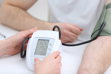 Doctor checking blood pressure of man in clinic, closeup