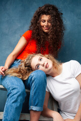 young pretty teenage girls friends with blond and brunette curly hair posing cheerful on blue background, lifestyle people concept