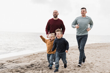Gay family having fun together on the beach in summer vacation - LGBT dads and sons lifestyle concept - Main focus on right man face