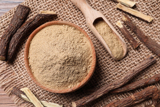 Dried sticks of liquorice root and powder on wooden table, flat lay