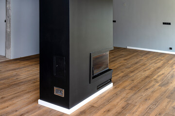 A modern fireplace with a closed combustion chamber standing in the living room, painted black, with a corner pane covered with soot.