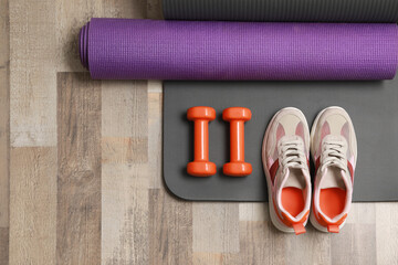 Dumbbells, sneakers and mats on wooden floor, flat lay. Space for text