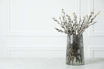 Beautiful pussy willow branches in glass vase on light grey marble table, space for text