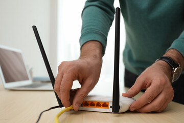 Man connecting cable to router at wooden table indoors, closeup. Wireless internet communication - obrazy, fototapety, plakaty