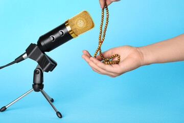 Woman making ASMR sounds with microphone and beads on light blue background, closeup