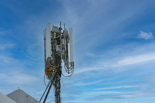 Engineer maintenance on telecommunication tower doing ordinary maintenance and control to antenna for communication, 4G and 5G cellular. Cell Site Base Station on blu sky background.