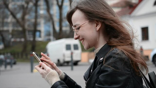 Side view of happy student girl in campus with a phone in her hands