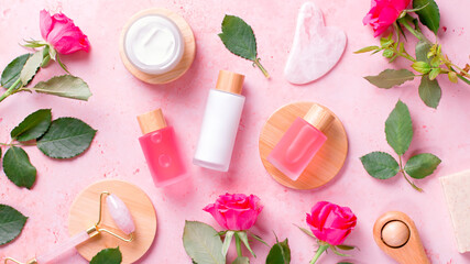 Obraz na płótnie Canvas Rose extract natural cosmetics in reusable bottles with gua sha facial beauty roller and natural rose flowers on pink, top view