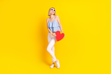 Full body photo of optimistic nice blond hair lady hold heart wear spectacles top pants isolated on yellow background