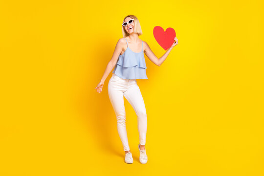 Full body photo of positive blond short hair lady hold heart wear spectacles top pants isolated on yellow background