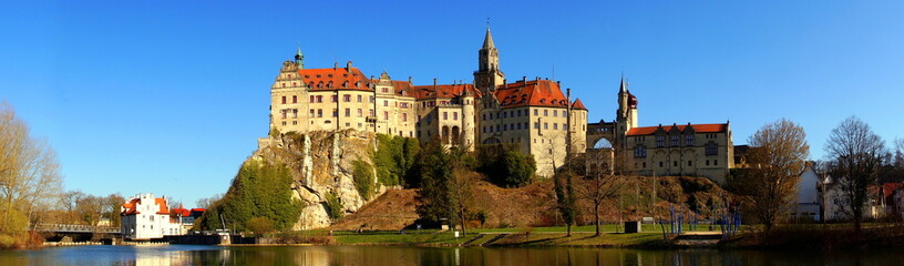 Fototapeta na wymiar weites Panorama von Schloss Sigmaringen unter blauem Himmel und Ufer der Donau mit Stauwehr