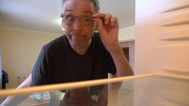 Hungry elderly man with funny face opens empty refrigerator