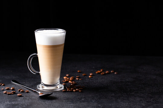 coffee with milk, latte macchiato in a glass with a handle and a long spoon on a black background, space for text