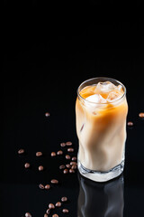 Ice coffee in a tall glass with cream poured over and coffee beans. Cold summer drink, vertical