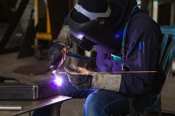 Welder is welding the steel in the factory. Weld the steel in dark. The welder has a protective device.