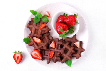 Chocolate waffles served with strawberry on ceramic plate on white table. Top view