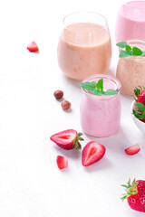 Pink and yellow smoothies topped with mint in glass jars on the white table. Healthy drink and kids food