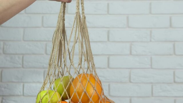 Fresh citrus in string bag. A view of a woman's hand with a string bag with different fruits in the room.