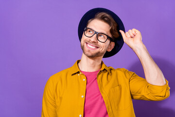 Photo of young handsome man happy positive smile hand touch hat dream look empty space isolated over violet color background