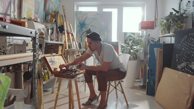 Zoom in shot of professional male artist sitting in creative studio and taking tools for painting from wooden case
