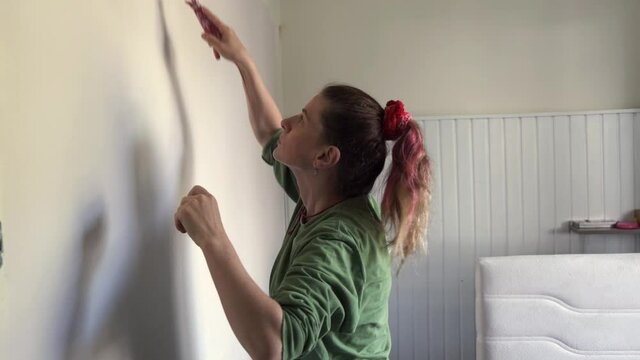 Footage of woman painting the room with roller brush