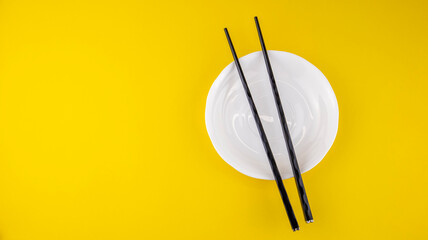 black chopsticks for sushi in a white saucer on a yellow background, isolated