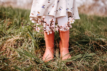 Closeup of a little girl standing in a garden with cherry tree flowers in rubber boots.